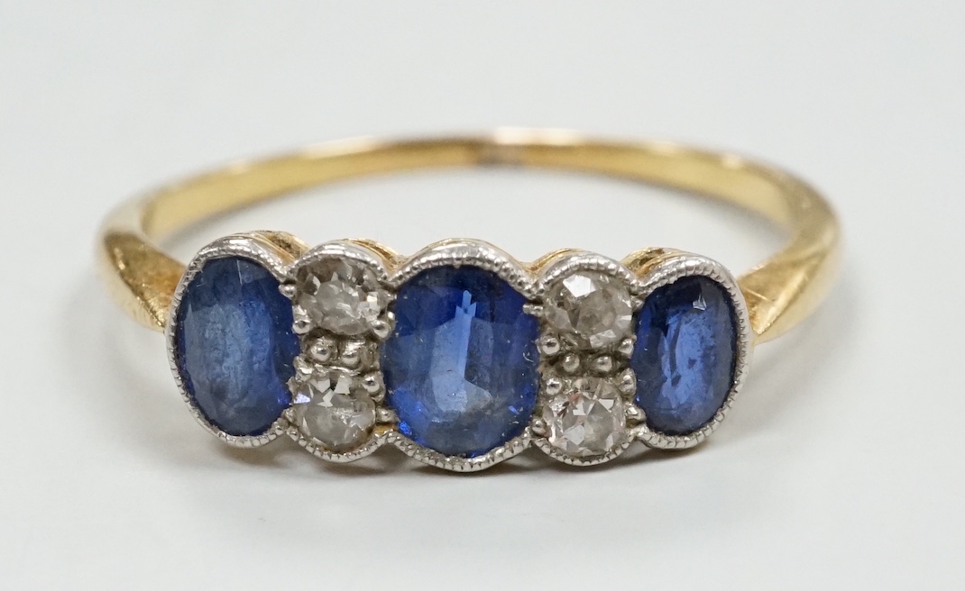 An early 20th century yellow metal and three stone oval cut sapphire set ring, with four stone diamond spacers, size O, gross weight 2 grams.